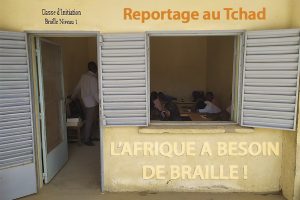 Photo : porte et fenêtre grandes ouvertes par lesquelles on voit une classe de braille, le professeur et ses élèves à N'Djamena.
