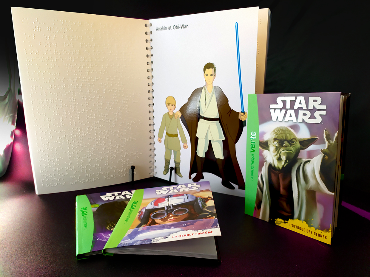 Photo livre en braille ouvert à la page illustration en relief d'Anakin et Obi-Wan Kenobi. Les 3 livres en noir de Star Wars sont devant.